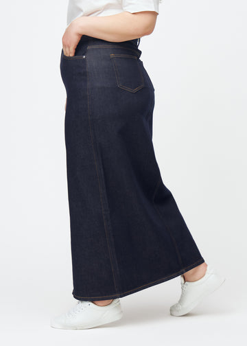 Long deep dark blue denim skirt for women in the colour Midnights seen from the side on a plus-size model, with a visible front slit.