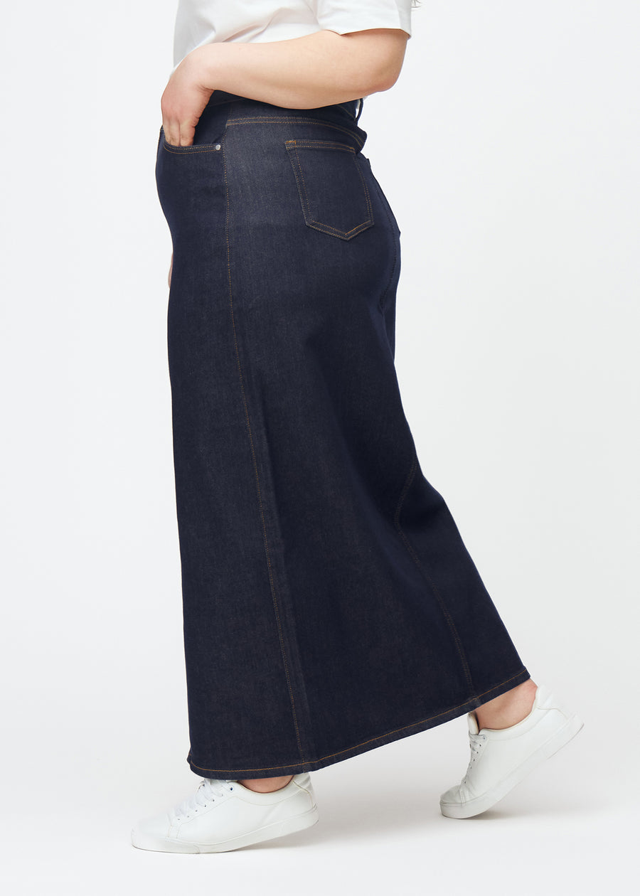 Long deep dark blue denim skirt for women in the colour Midnights seen from the side on a plus-size model, with a visible front slit.