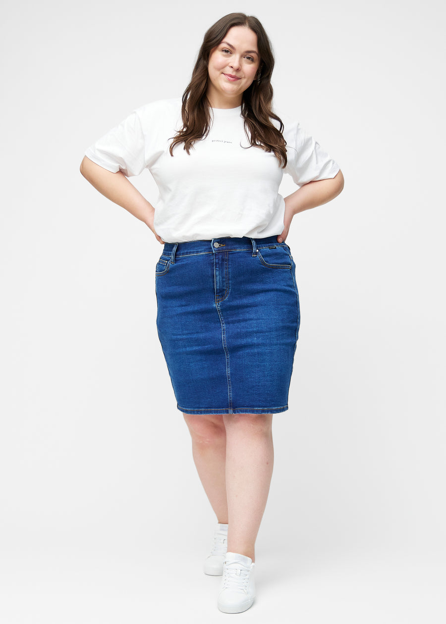 Fuldt billede af plus-size model i mørkeblå, tætsiddende og knælang denimnederdel.