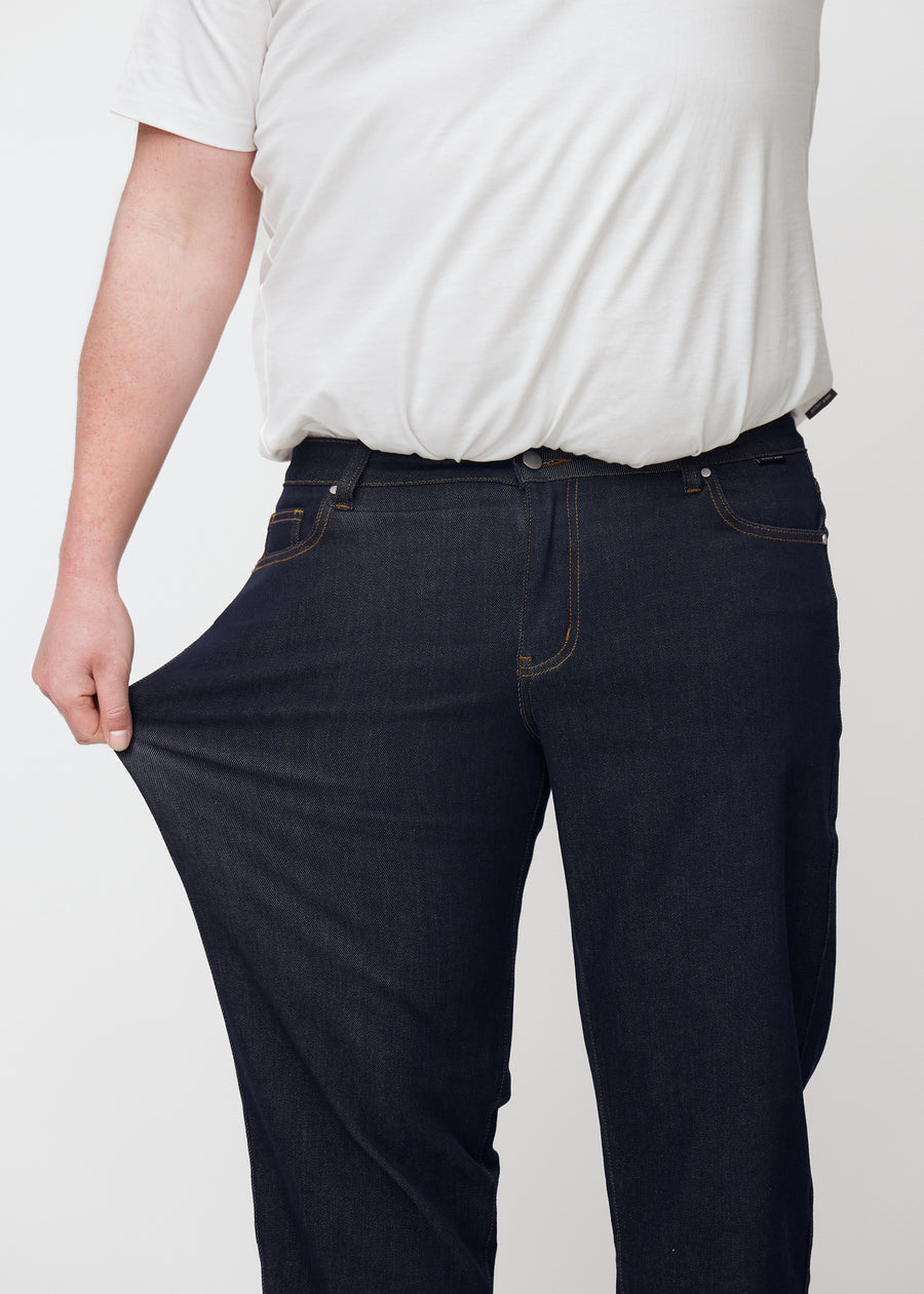 The plus-size model stretches the deep dark blue denim jeans for men in the color Midnights at the thigh to show the material&