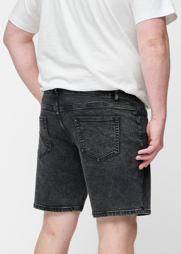 Plus-size model stretches the dark grey denim shorts for men in the colour Shadows at the thigh to show the stretch of the material.