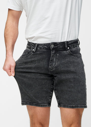 Model stretches the dark grey denim shorts for men in the colour Shadows at the thigh to show the stretch of the material.