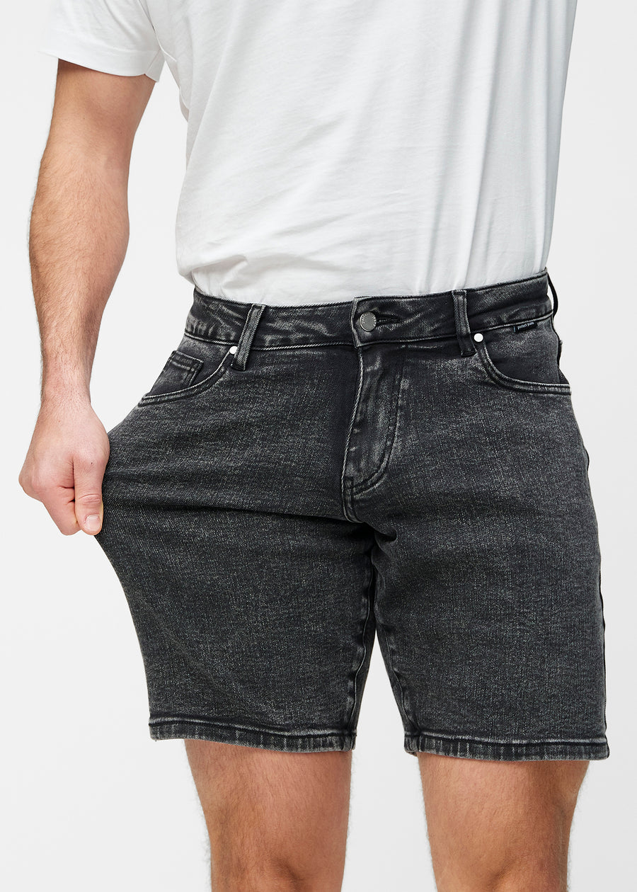 Model stretches the dark grey denim shorts for men in the colour Shadows at the thigh to show the stretch of the material.