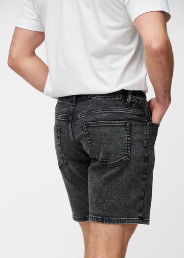 Model stretches the dark grey denim shorts for men in the colour Shadows at the thigh to show the stretch of the material.