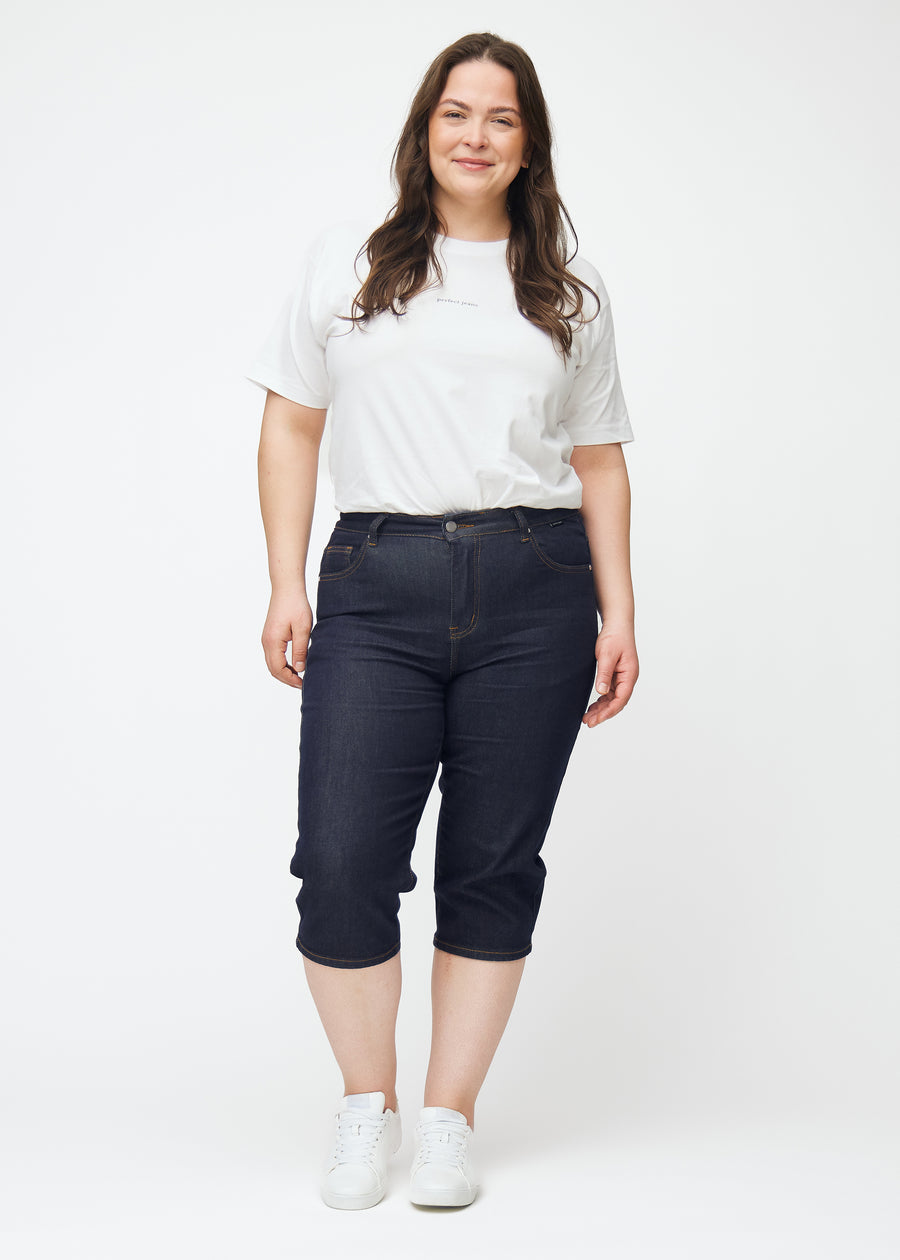 Plus-size model viser dyb mørkeblå denim capris til kvinder i farven Midnights med slim pasform i bevægelse.