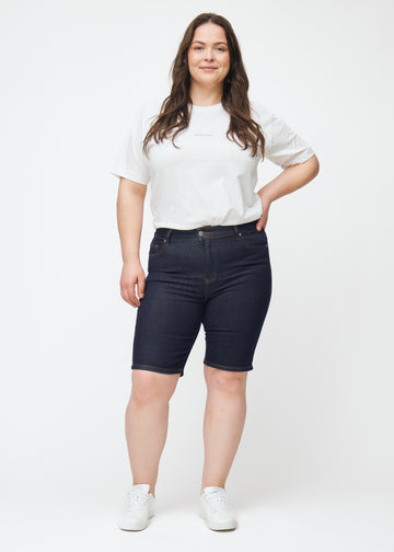 Plus-size model viser dyb mørkeblå denim shorts til kvinder i farven Midnights med skinny pasform i bevægelse.