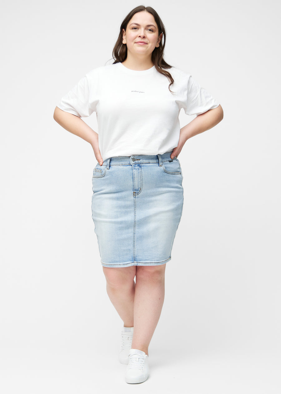 Plus-size model viser lyseblå, tætsiddende og knælang denimnederdel i bevægelse og strækker materialet.
